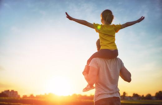 Child on dad's shoulders watching sunset