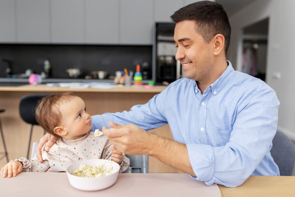 Dad feeds baby breakfast at the kitchen table