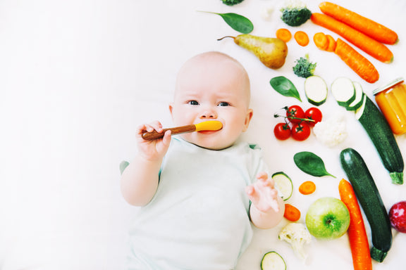 Healthy child nutrition, food background, top view. Baby 8 months old surrounded with different fresh fruits and vegetables on white background. Baby first solid feeding