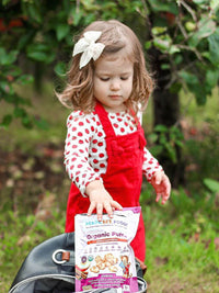 Child in red dungarees holding bag of RSF! Organic Puffs