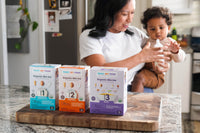 Mom holding baby in kitchen with boxes of RSF! Mix-Ins in the foreground